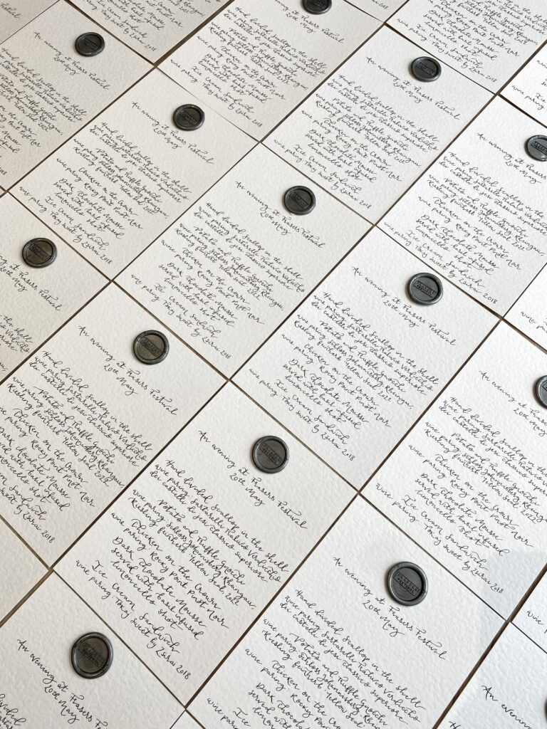 An A5 handwritten calligraphy menu on white paper with black ink, featuring a branded wax stamp on each one